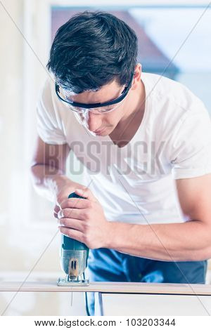DIY worker cutting wooden panel with jig saw
