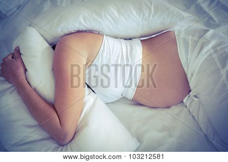 High angle view of pregnant woman with headache lying on bed with pillow