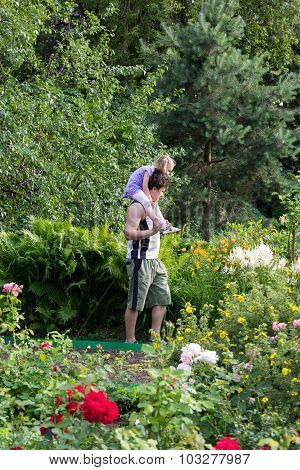 Little Girl Sitting On The Daddy Shoulders Among Flowers