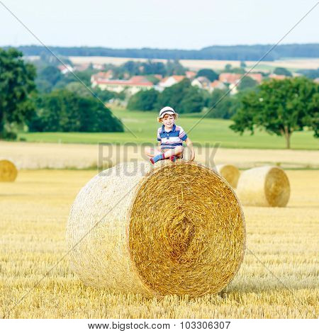 Little Kid Boy Sitting On Hay Bale In Summer