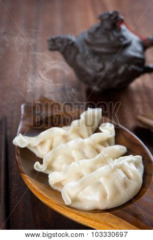 Fresh dumplings with hot steams on wood plate. Delicious Chinese gourmet on rustic old vintage wooden background. 