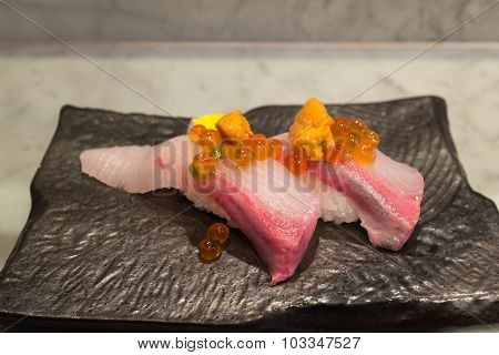 Kampachi sushi with Uni and Ikura on top on black ceramic plate
