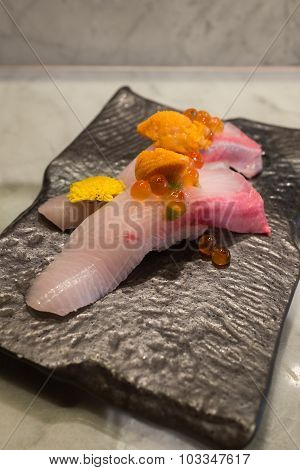 Kampachi sushi with Uni and Ikura on top on black ceramic plate