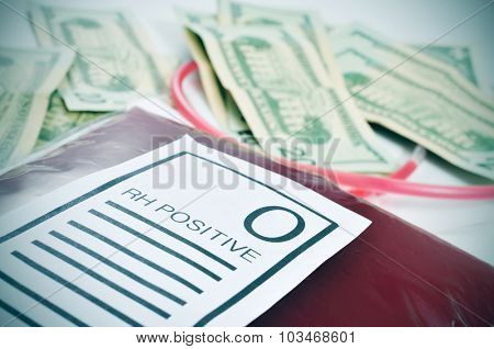 closeup of a blood bag with a label with the text O RH positive and a pile of US dollar bills in the background