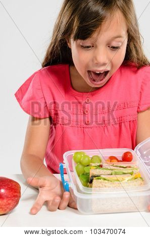 Young girl is excited about her healthy packed lunch with wholemeal ham sandwich and fresh fruit