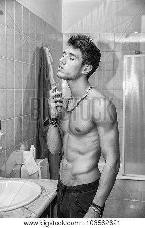 Handsome young man in bathroom, spraying cologne or perfume