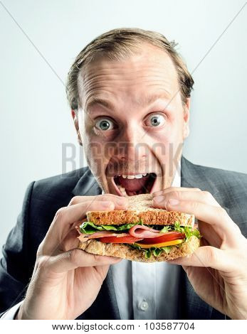 Business man in suit with wide open mouth and eyes eating his healthy lunch sandwich, comical funny image with split tone grading