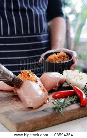 Home chef marinating seasoning raw chicken breasts with a spice mixture rub, preparing for a barbeque