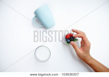 Hand Gently Takes One Berry From Jar Filled With Various Berries On White Table