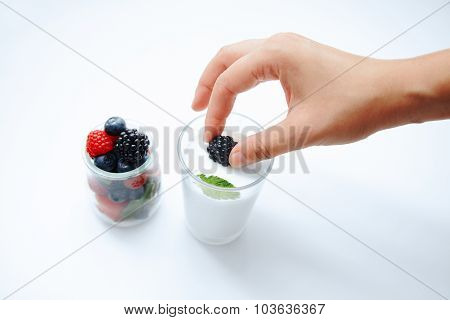 Hand Gently Puts One Berry From Jar Filled With Various Berries To Glass With Milk