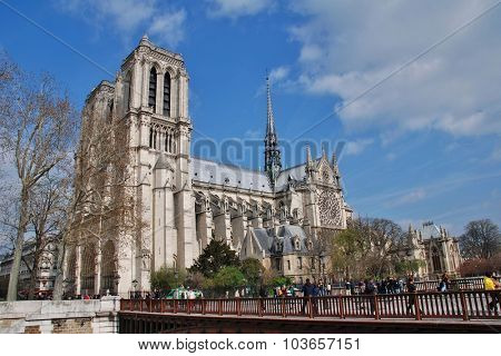 PARIS, FRANCE - MARCH 18, 2014: People walk across the Pont au Double in front of the historic Notre Dame cathedral. Started in 1120, the Catholic cathedral was completed in 1345.