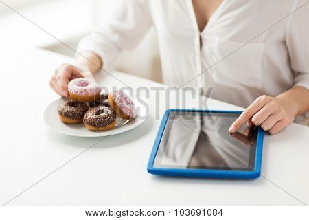 people, junk food, diet, technology and unhealthy eating concept - close up of hands with tablet pc computer and donuts counting calories and sitting at table at home