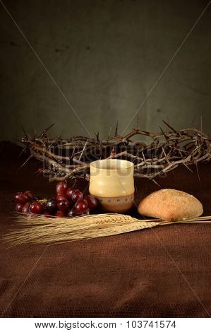 Table with cup of wine, bread, grapes, wheat, and crown of thorns