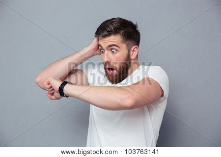 Portrait of a shocked man looking on wrist watch over gray background