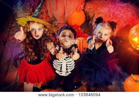 Three children dressed as a witch, a skeleton and a black cat celebrating halloween in a wooden barn with pumpkins. Halloween concept.
