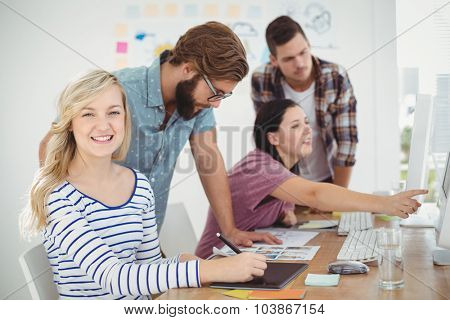 Portrait of smiling woman using digital tablet with coworkers working at computer desk