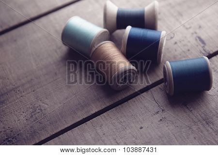 Old sewing thread wooden reels or bobbins on a old rustic work bench. Intentionally shot in muted retro-vintage tone and shallow depth of field. (soft focus)