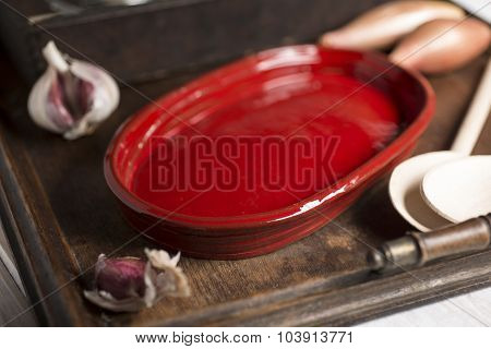 Red Shallow Dish, Spoons, And Garlic In Wooden Tray