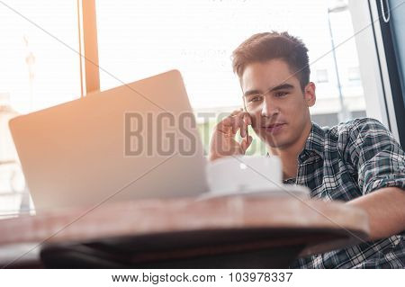 Businessman Using Mobile Phone While Lookingat Laptop On Wooden Table In Coffee Shop