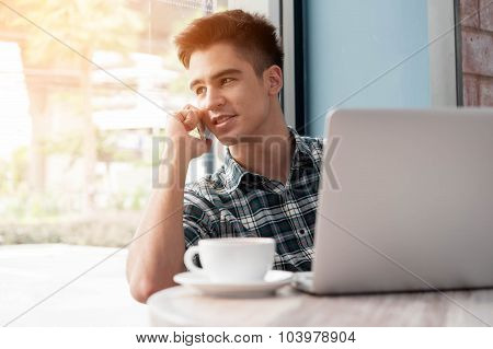Businessman Using Mobile Phone While Lookingat Laptop On Wooden Table In Coffee Shop