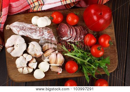 Salami With Cherry Tomatoes, Pepper, Garlic And Ruccola On A Cutting Board