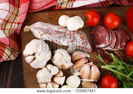 Salami With Cherry Tomatoes, Ruccola And Garlic On A Cutting Board