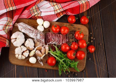 Salami With Cherry Tomatoes, Ruccola And Garlic On A Cutting Board
