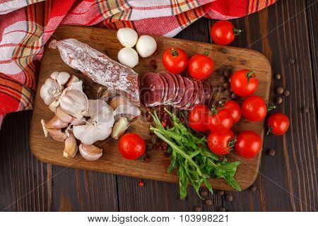Salami With Cherry Tomatoes, Ruccola And Garlic On A Cutting Board