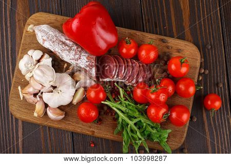 Salami With Cherry Tomatoes, Pepper, Garlic And Ruccola On A Cutting Board