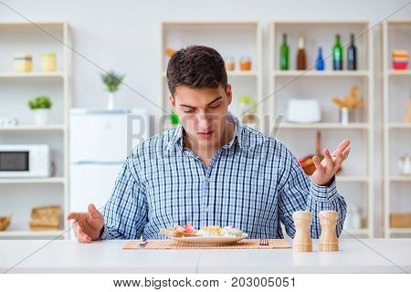Young husband eating tasteless food at home for lunch