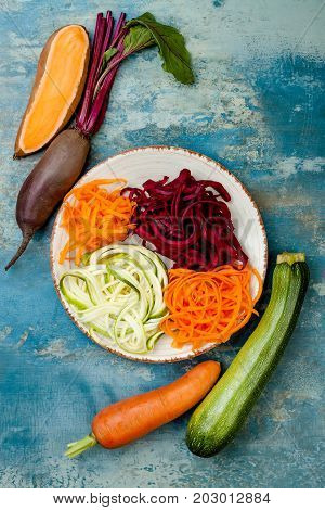 Zucchini carrot sweet potato and beetroot noodles on a plate. Top view overhead. Blue rustic background