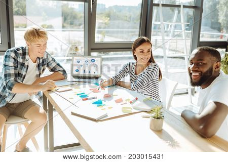 New business idea. Cheerful group of young people discussing new start up trands and sititng at the table while working together