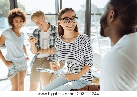 Happy youth. Cheerful international students talking while their groupmates standing in the background and using modern gadgets