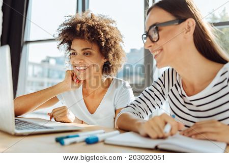 Distance learning. Cheerful smiling young female students using the laptop and studying while expressing gladness