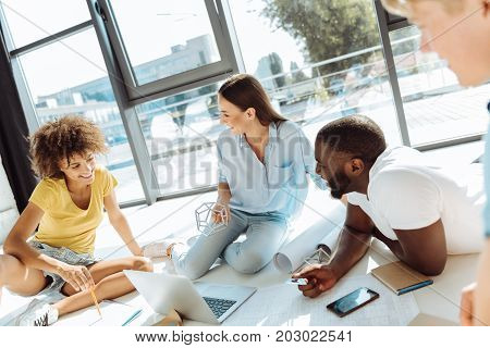 Mind exchange. Joyful smart international students sitting on the floor and talking while getting ready with the university project