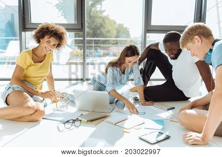 Project in progress. Cheerful enthusiastic international students sitting on the floor and studying while preparing their university work