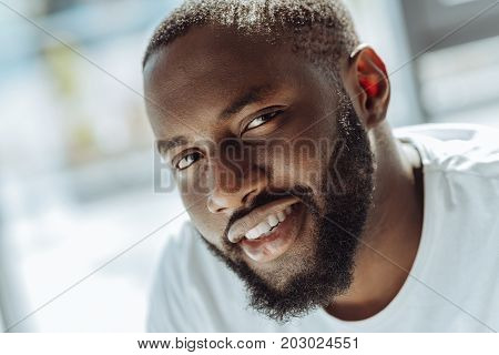 Respect my ethnical background. Close up of a cheerful young afro american man smiling and looking at you while expresing joy