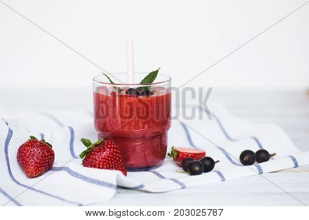 Smoothies of black currant and strawberries with yogurt on a white wooden table.