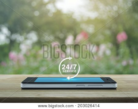 24 hours service icon on modern smart phone screen on wooden table over blur pink flower and tree Full time service concept