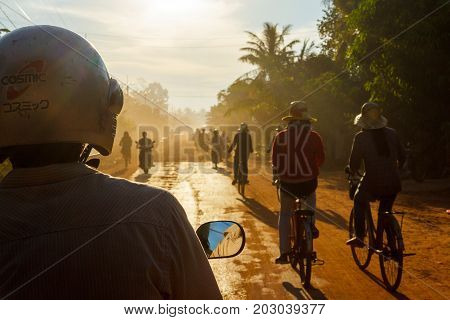 SIEM REAP CAMBODIA - SEPTEMBER 5 2015: Riding in a tuk-tuk while others bicycle and motorbike down a countryside dirt road.