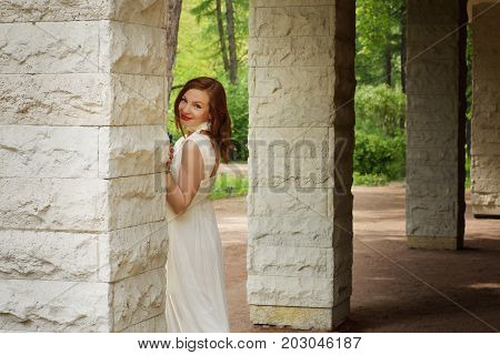A girl in a white dress peeks out from behind a column.