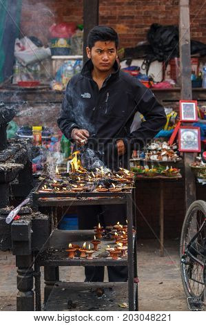 KATHMANDU NEPAL - 9/26/2015: A candle salesman smokes a cigarette at Durbar Square during the Indra Jatra festival in Kathmandu Nepal.