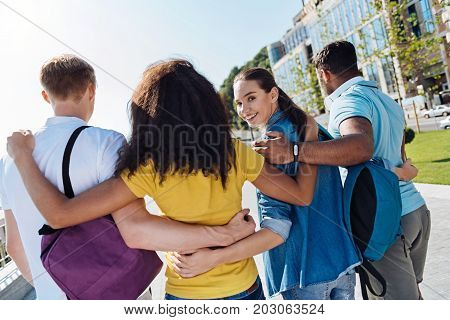 Keep smiling. Charming girl expressing positivity and embracing her friends while turning head