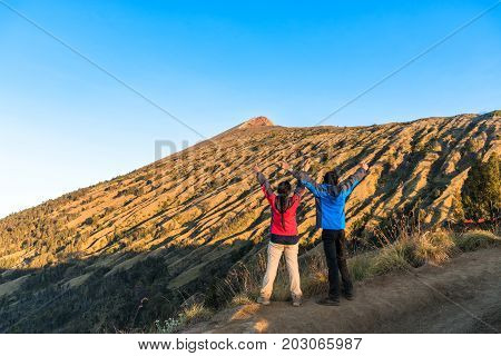 Young man and woman hiker spreading hand enjoy and happy with mountain top view after finished climbing at Rinjani mountain Lombok Indonesia.