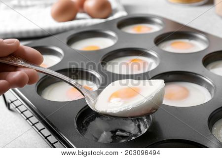 Woman holding spoon with baked egg over muffin tin
