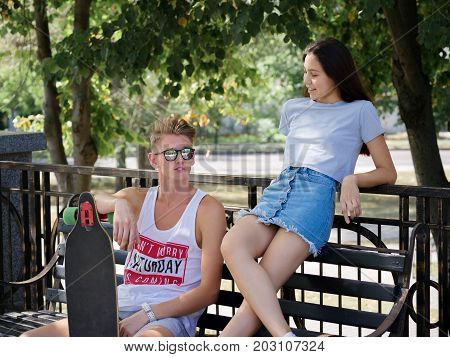A beautiful girl sitting with a fellow on a bench in a park, dating in a park on a blurred natural background. Love, date, dating, outdoor, park, nature concept.