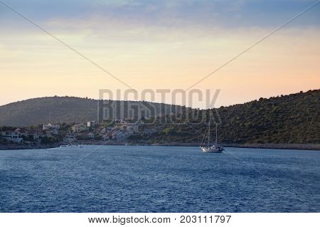 Sailboat in blue bay with romantic town on island. Luxury sail yacht in azure sea on roadstead.