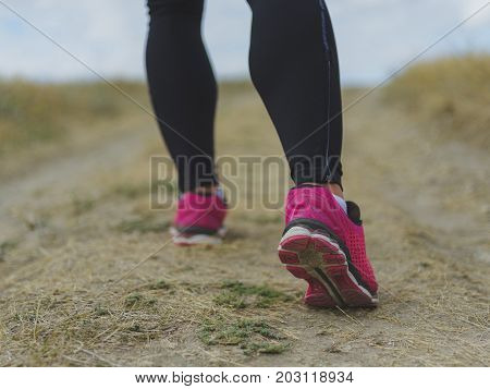 Close-up picture of fit, sporty, muscular legs running on a blurred light natural background. Man walking in black leggings and sneakers. Marathon, jogging, running, training, exercising concept.