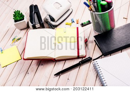 Top view workspace mockup on wooden background with blank notebook with copy space, pen, tacker, punch, clips and accessories. Overhead view. Flat lay, top view