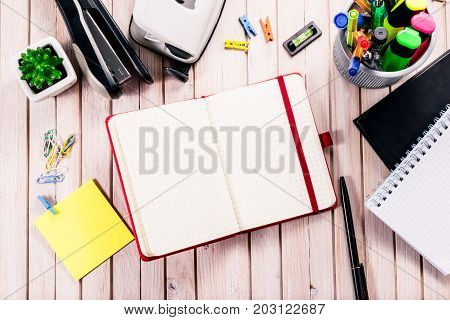 Top view workspace mockup on wooden background with blank notebook with copy space, pen, tacker, punch, clips and accessories. Overhead view. Flat lay, top view